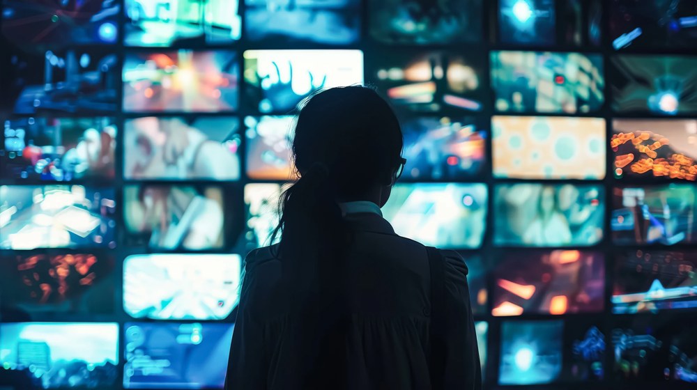 Person vor einer Wand aus Medienmonitoren